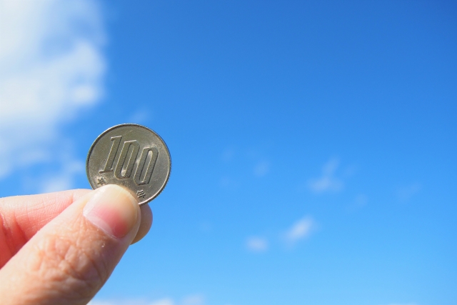 青空の下、一枚の百円硬貨をかざす手