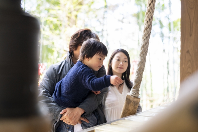 三人の親子連れ。パパに抱えられた子どもがお賽銭を入れようとしている。