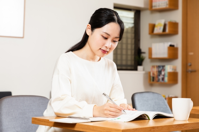 テーブルに向って書きものをする若い女性