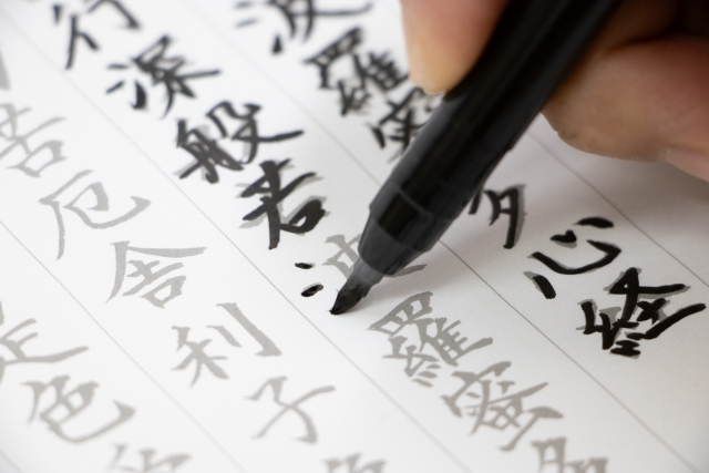 薄く下書きのお手本が書いてある半紙に、なぞりながら写経をしている手。